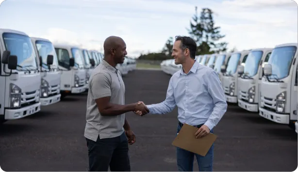 Two men shaking hands in lot of box trucks